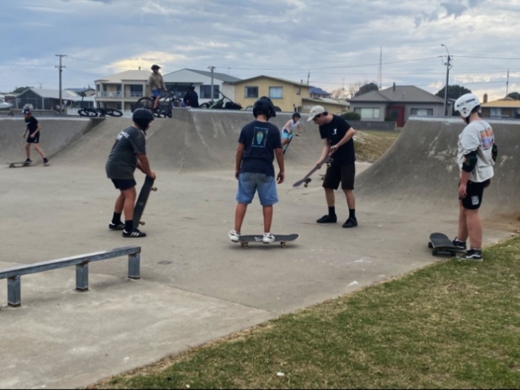 4 young people learning to ride skateboards with an instructor. One is riding the board and the others are about to start.