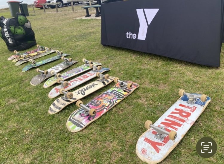 A collection of decorated skateboards lying on the grass next to a YMCA table at the Port MacDonnell Skate Park.
